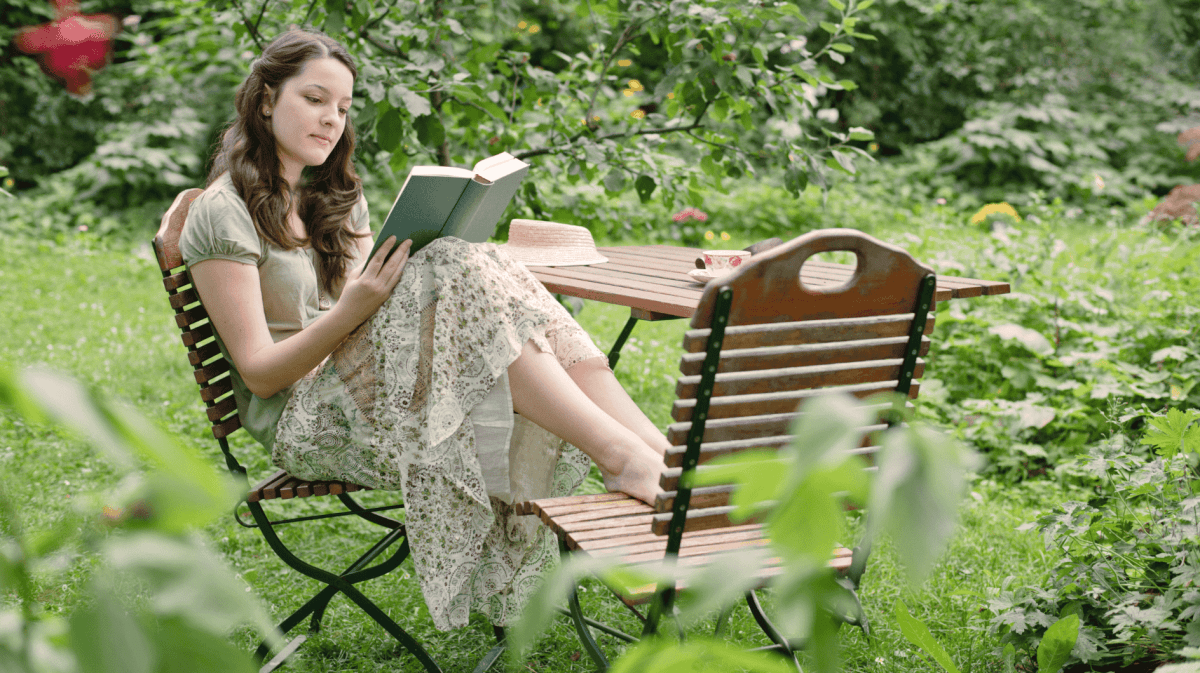 Frau sitzt in ihrem Garten und liest ein Buch.