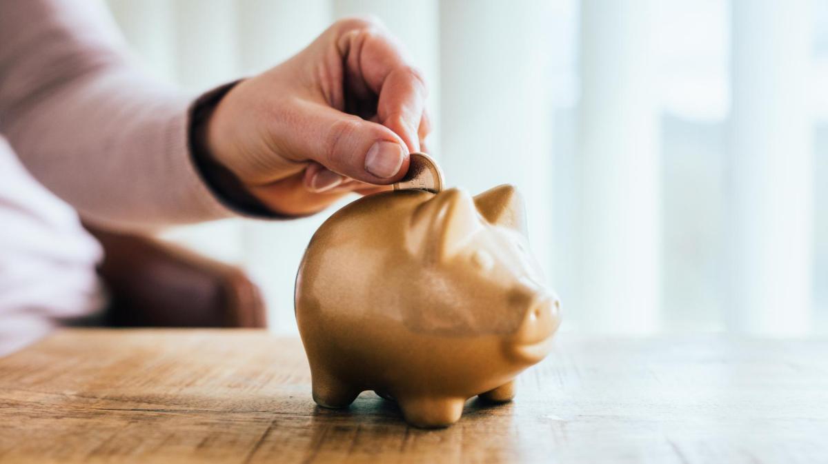 Person wirft Geldmünze in ein goldenes Sparschwein.
