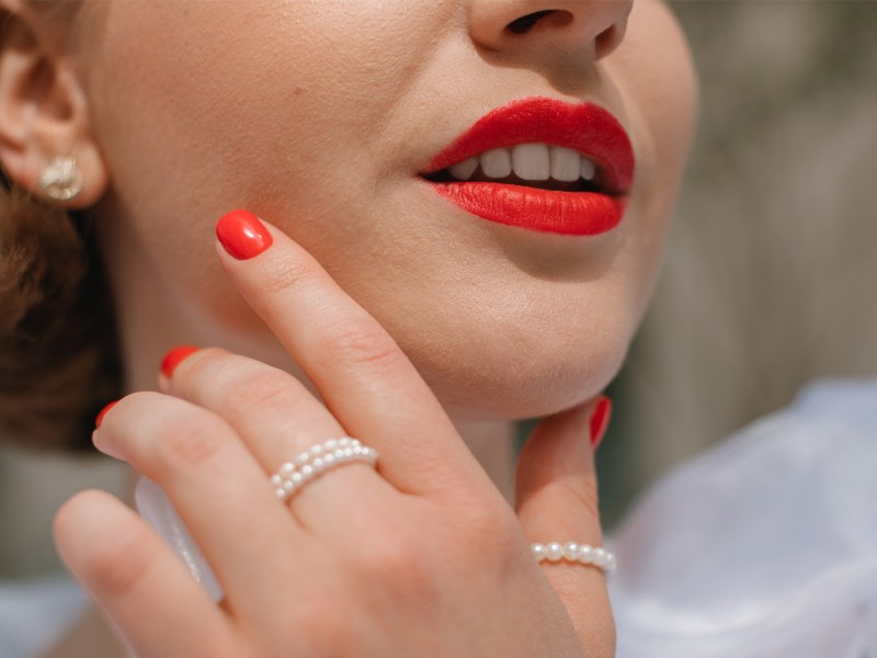 Frau mit hellrot lackierten Fingernägeln und passendem Lippenstift