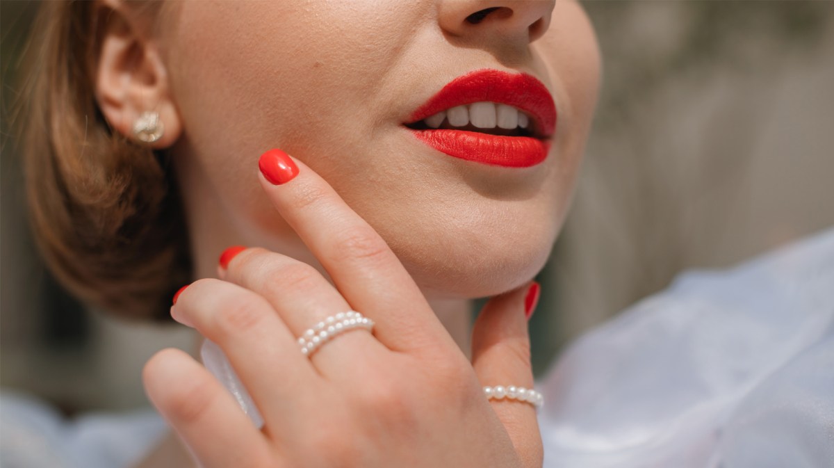 Frau mit hellrot lackierten Fingernägeln und passendem Lippenstift