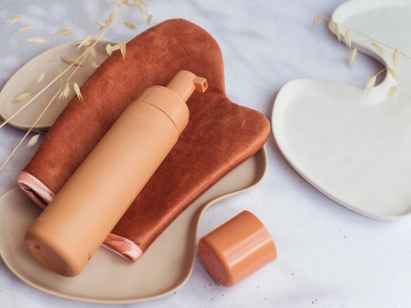 Braune Flasche mit Selbstbräuner, die auf einem speziellen Tanning-Handschuh liegt