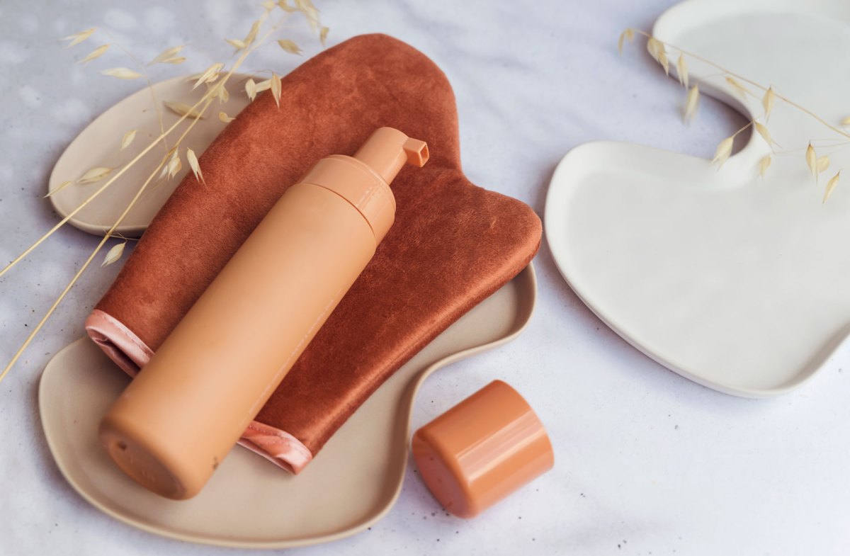 Braune Flasche mit Selbstbräuner, die auf einem speziellen Tanning-Handschuh liegt