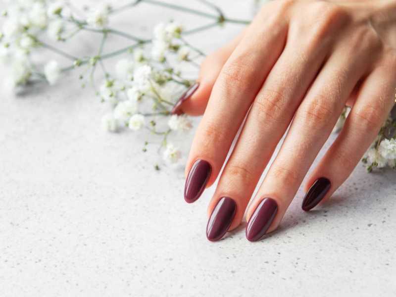 Rot lackierte Fingernägel vor weißen Blumen
