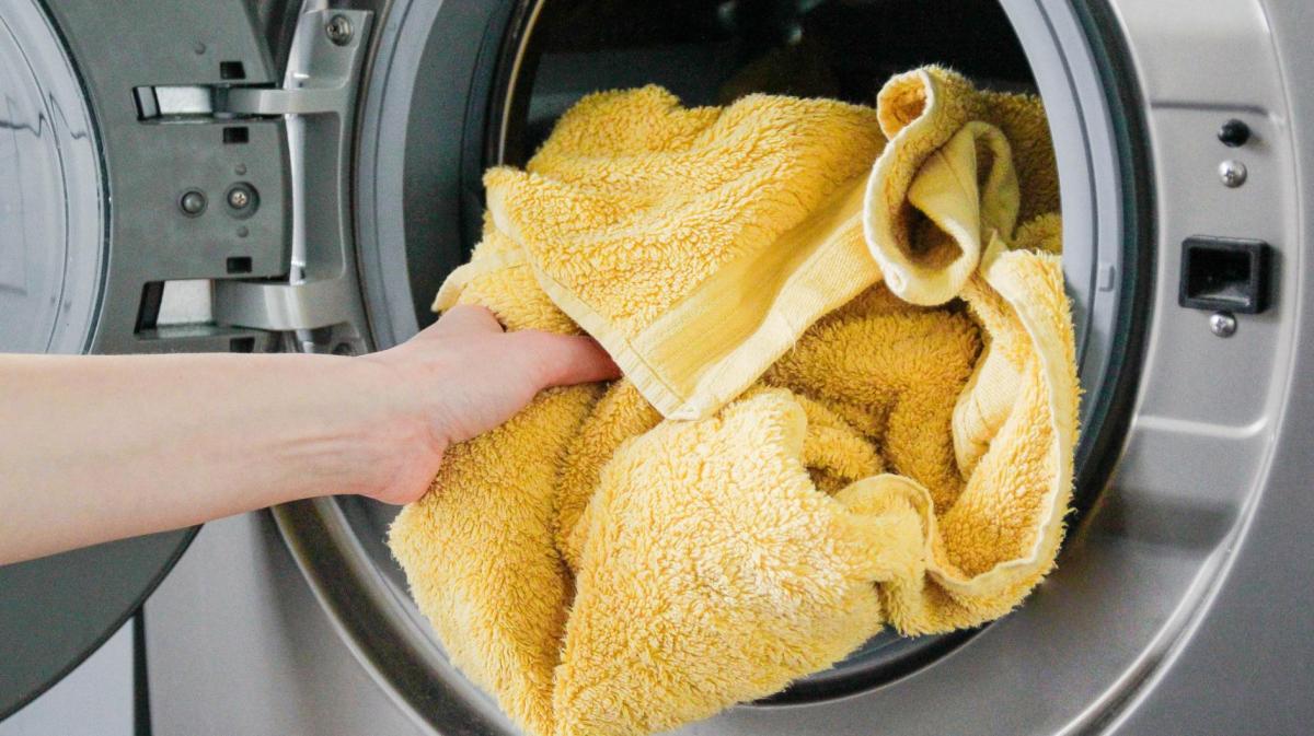 Person wirft ein gelbes Handtuch in die Waschmaschine.