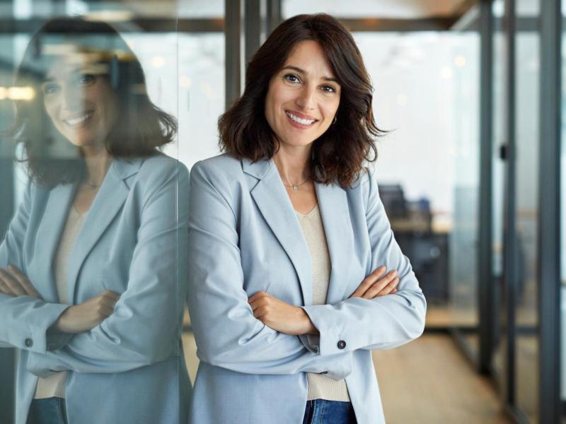 Frau mit Blazer und dunklen Haaren steht im Büro.