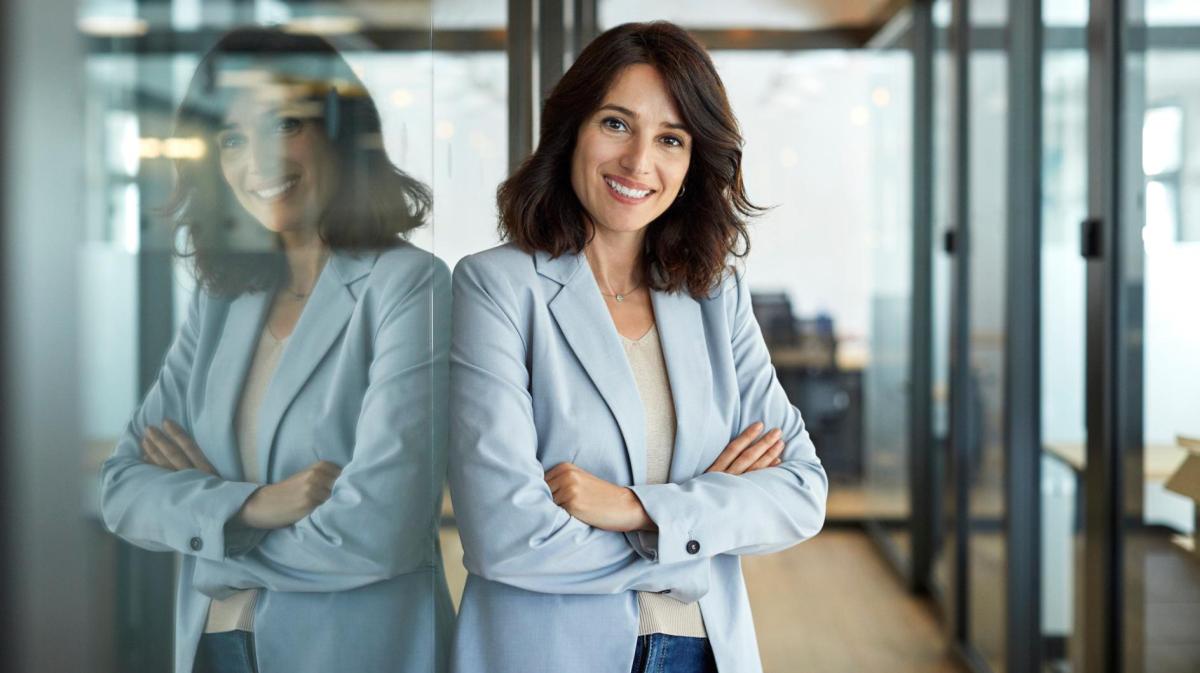 Frau mit Blazer und dunklen Haaren steht im Büro.
