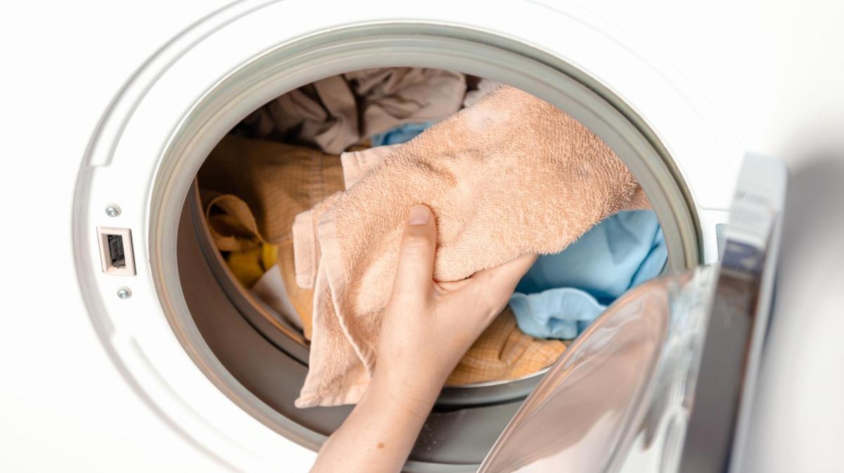 Eine Hand gibt Handtücher in eine Waschmaschine.