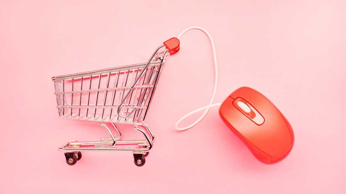 Einkaufswagen und rote Computermaus auf rosa Hintergrund.