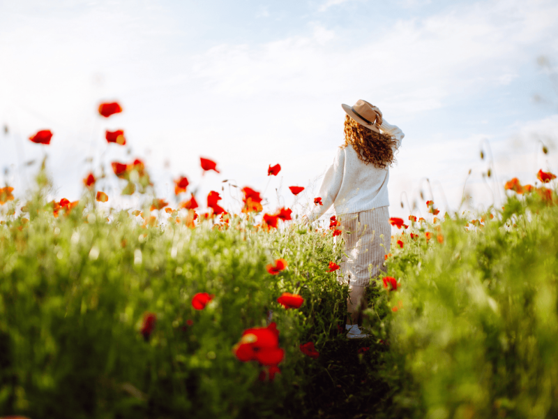 Frau mit roten Haaren läuft durch ein Feld mit Klatschmohn.