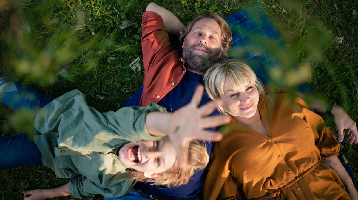 Mutter, Vater und Kind liegen auf einer Picknickdecke auf dem Rasen.