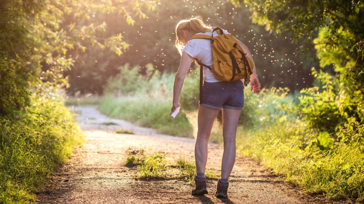Frau auf einem Waldweg im Sommer, die sich mit Insektenschutz einsprüht.