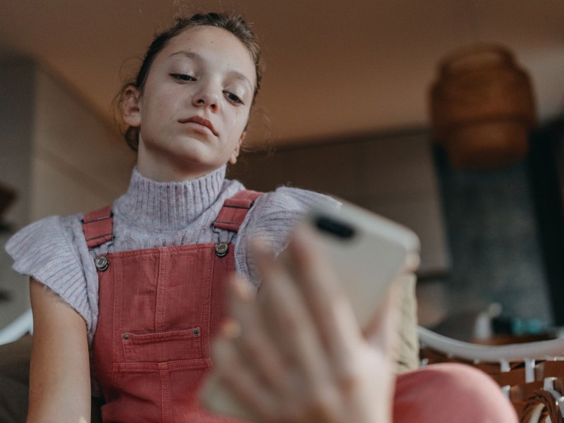 Mädchen im Teenageralter sitzt auf dem Sofa und schaut genervt auf ihr Smartphone.