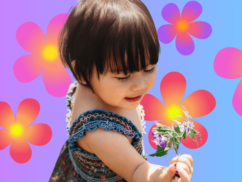Kleinkind mit Kleid steht auf einer Wiese und hält eine Blume in der Hand.