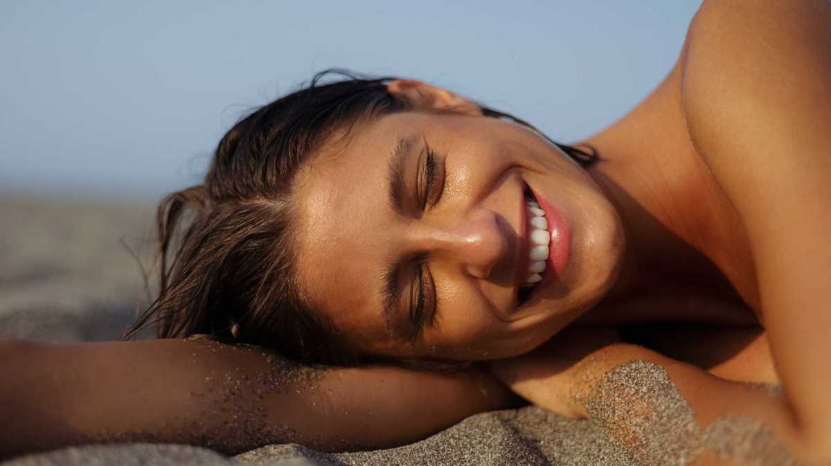 Junge Frau mit einem gebräunten Teint liegt im Sommer an einem Strand.