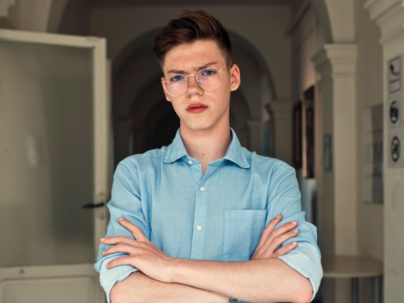 Porträt eines Teenagers, der mit verschränkten Armen und böse Blick im Flur einer Wohnung steht.