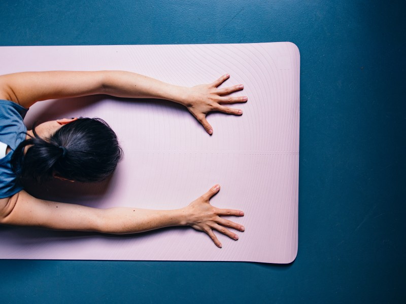 Frau macht auf rosa Sportmatte Yoga und streckt die Arme aus