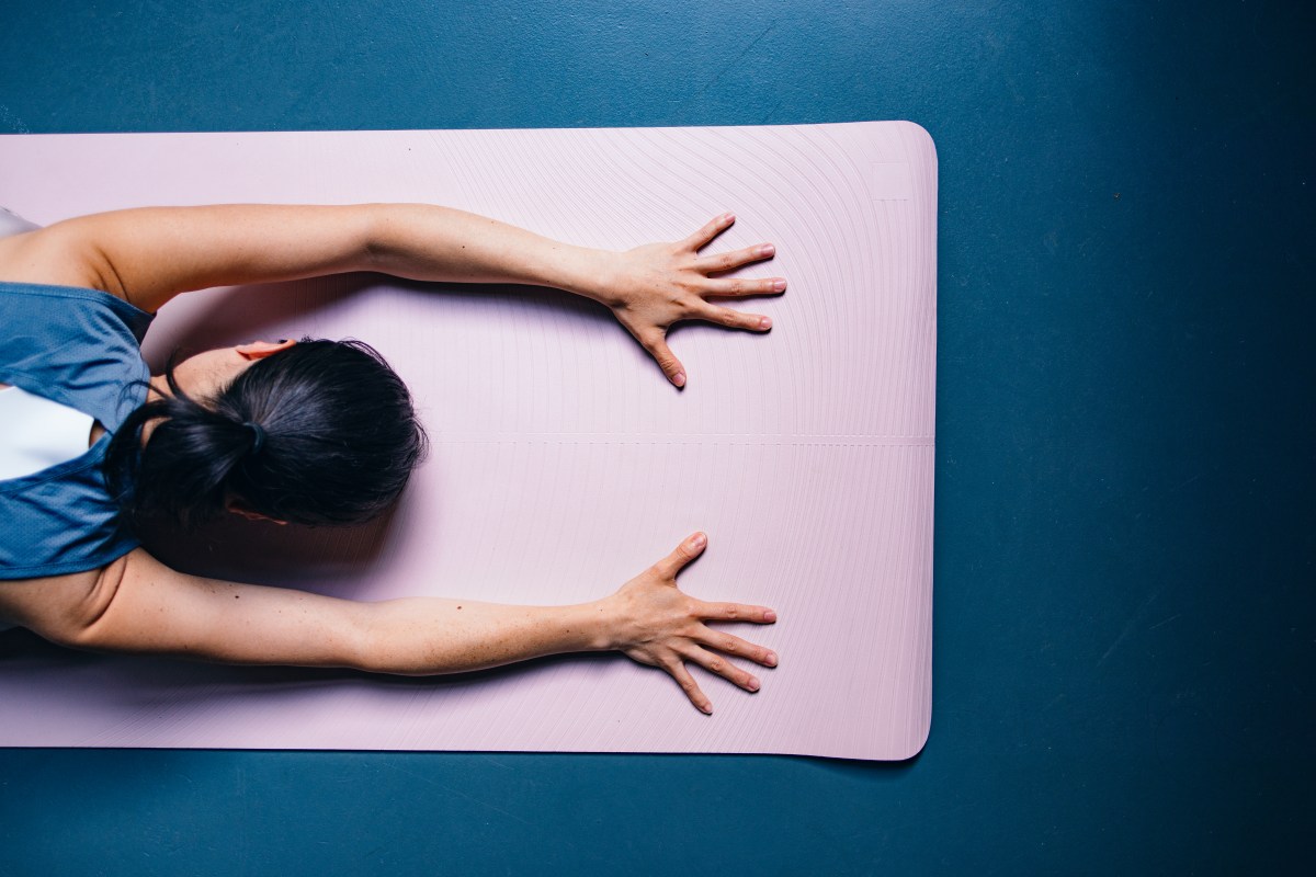 Frau macht auf rosa Sportmatte Yoga und streckt die Arme aus