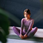 Schlanke Frau mit lila Sportkleidung sitzt auf Yogamatte