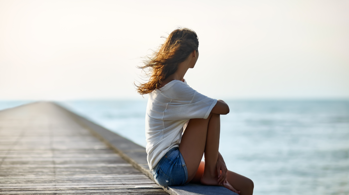 Frau in einem weißen T-Shirt sitzt auf einem Holzsteg am Meer