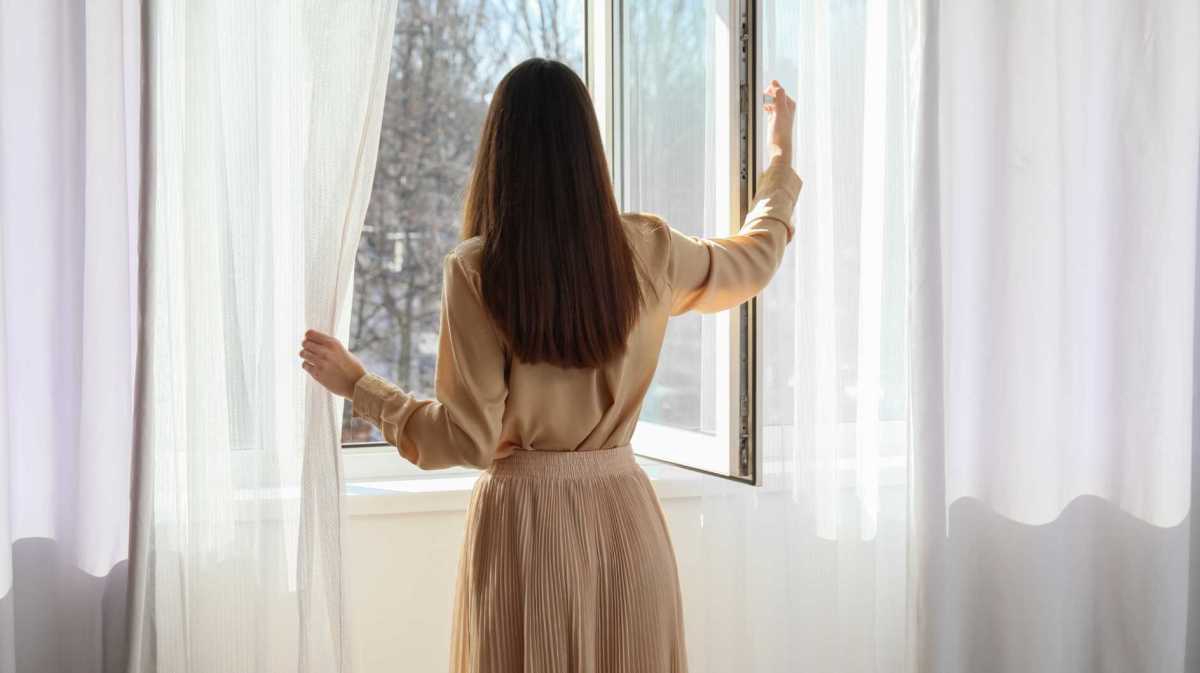 Frau steht vor dem Fenster und lüftet