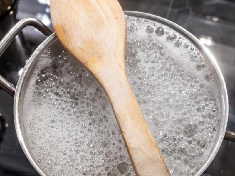 Holzlöffel liegt auf einem Topf mit kochendem Wasser.