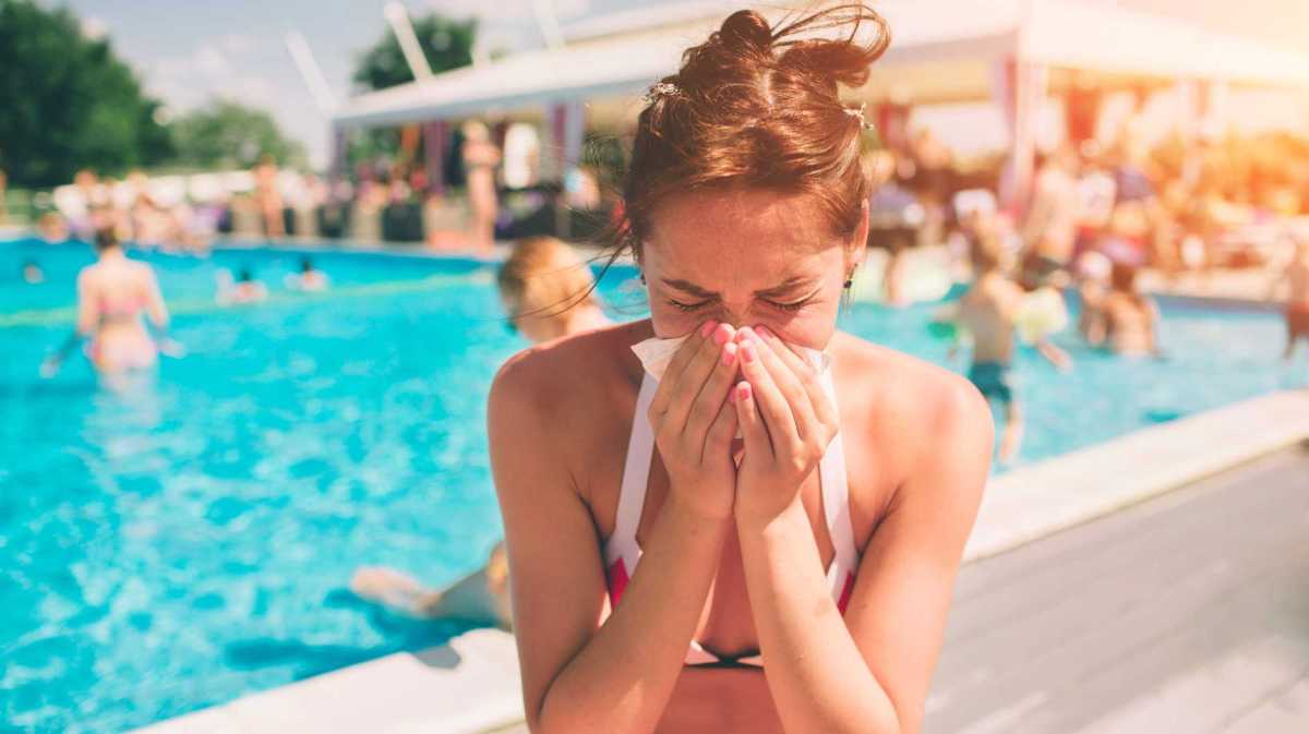 Frau sitzt krank am Pool im Bikini und schnäuzt sich die Nase