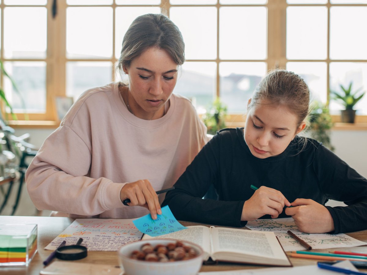 Mädchen und Mutter sitzen am Tisch und arbeiten Material durch.