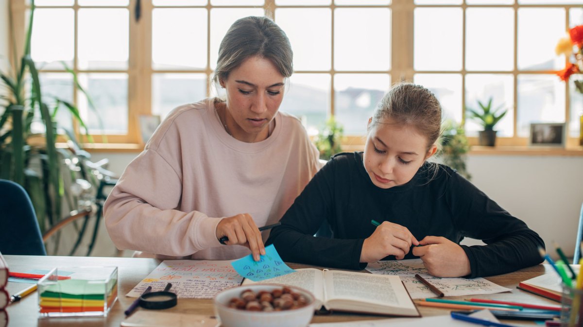 Mädchen und Mutter sitzen am Tisch und arbeiten Material durch.