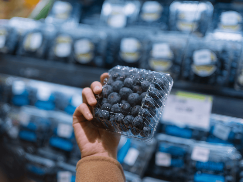 Frau hält im Supermarkt eine Schale Blaubeeren in der Hand.