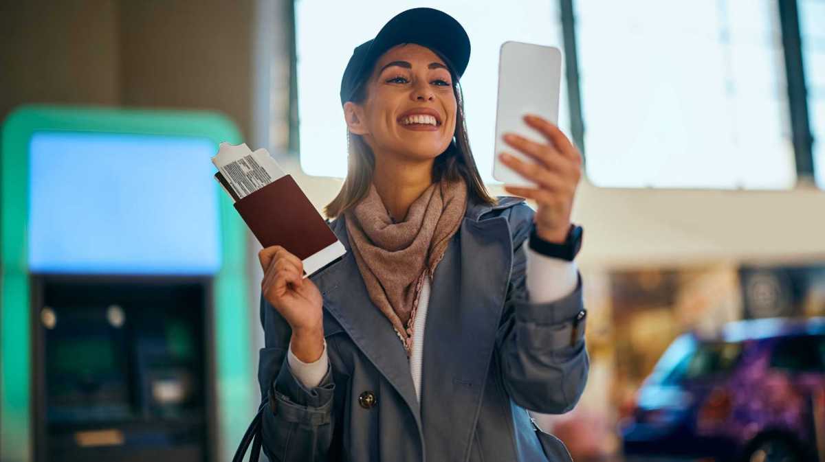 Junge Frau macht ein Selfie am Flughafen mit ihrem Boardingticket.