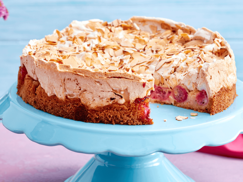 Stachelbeerkuchen mit Baiserhaube auf blauem Kuchenständer.