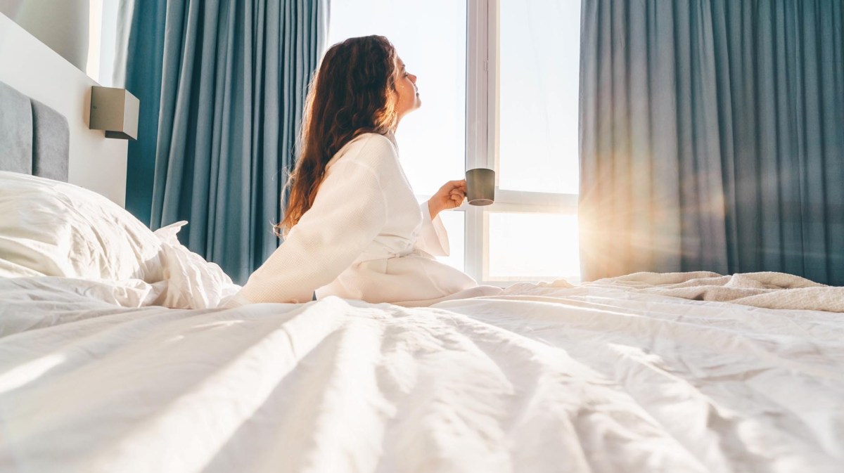 Frau liegt im Hotelzimmerbett im Urlaub und trinkt Kaffee