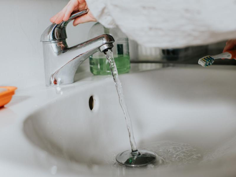 Frau dreht Wasserhahn an einem Waschbecken auf.