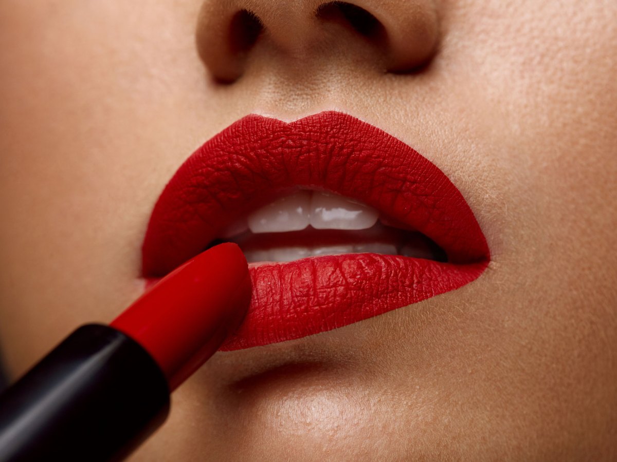 Frau mit perfekt geschminkten roten Lippen, die gerade einen Lippenstift aufträgt.