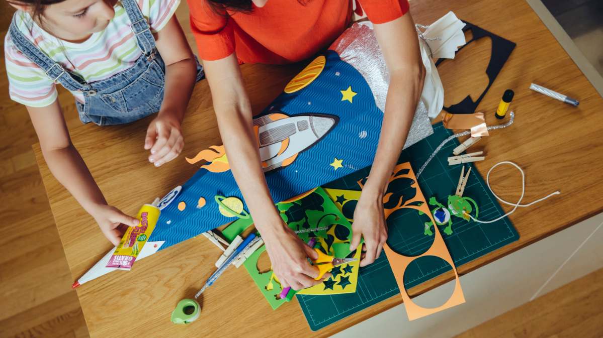 Mutter und Tochter stehen am Tisch und basteln eine Schultüte.
