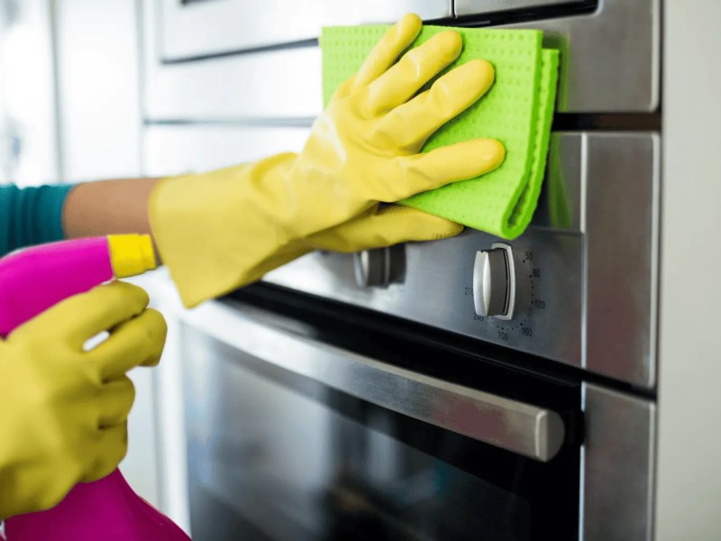 Person mit gelben Putzhandschuhen wischt über Ofen.