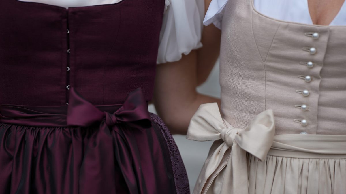 Zwei Frauen im Dirndl stehen eng nebeneinander, die Schleifen ihrer Schürzen sorgfältig vorne gebunden.