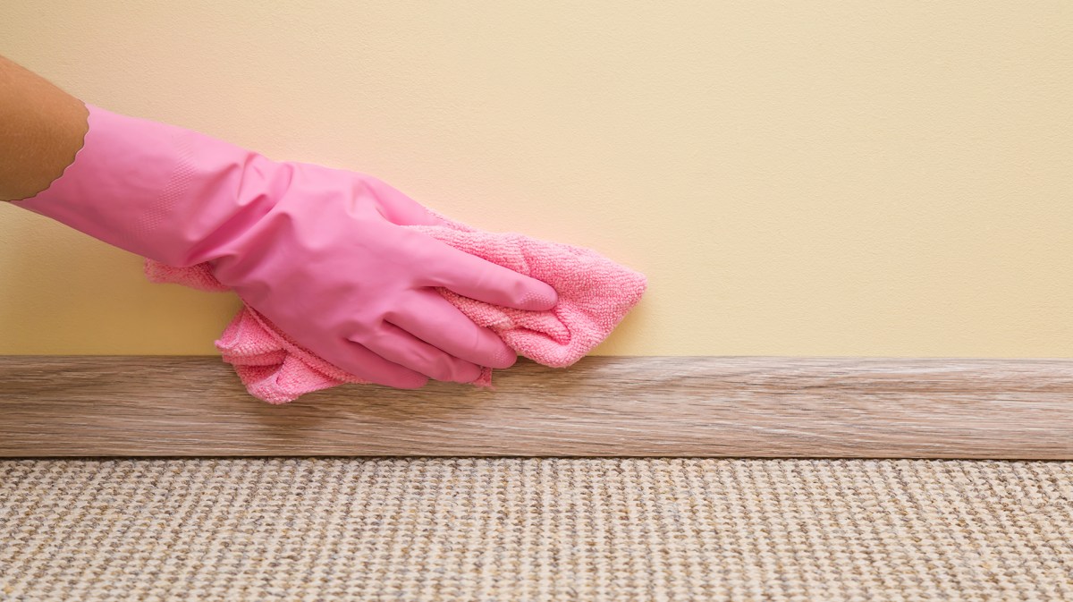 Frau trägt pinkfarbene Handschuhe zum Putzen der Fußleisten mit einem blauen Tuch