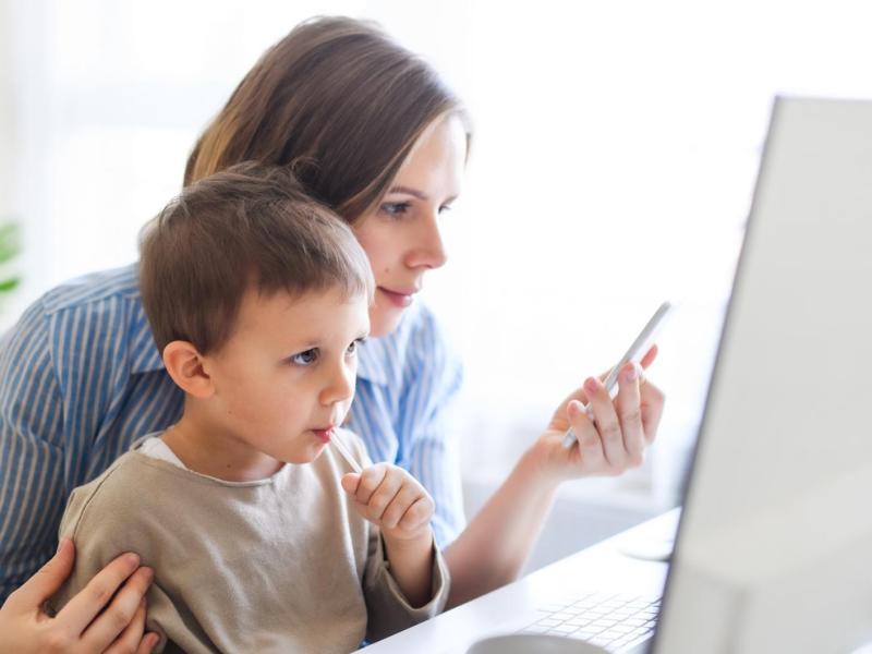 Mutter sitzt mit ihrem Kind vor dem PC und arbeitet.