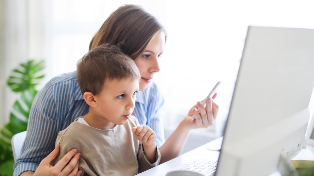 Mutter sitzt mit ihrem Kind vor dem PC und arbeitet.