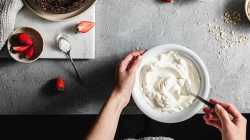 Pov-Aufnahme einer Köchin, die Joghurt in einer Schüssel in der Küche mit Zutaten auf der Küchentheke mischt.