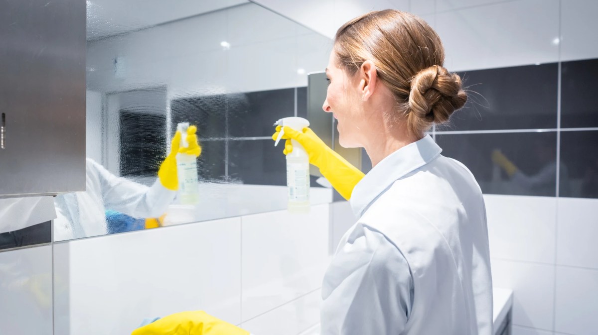 Eine blonde Frau sprüht einen Badezimmerspiegel ein