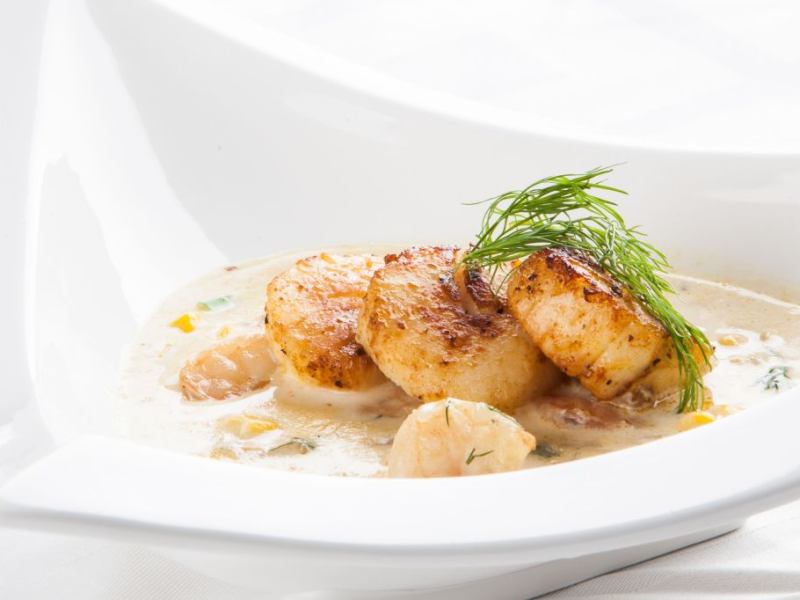 Suppe mit Jakobsmuscheln in einer weißen Schüssel.